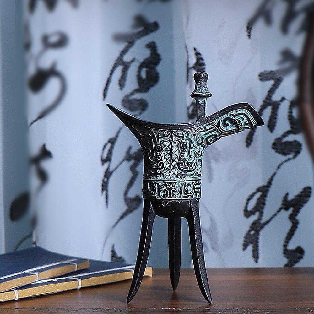 Small bronze Jue cup displayed beside stacked books as a scale reference