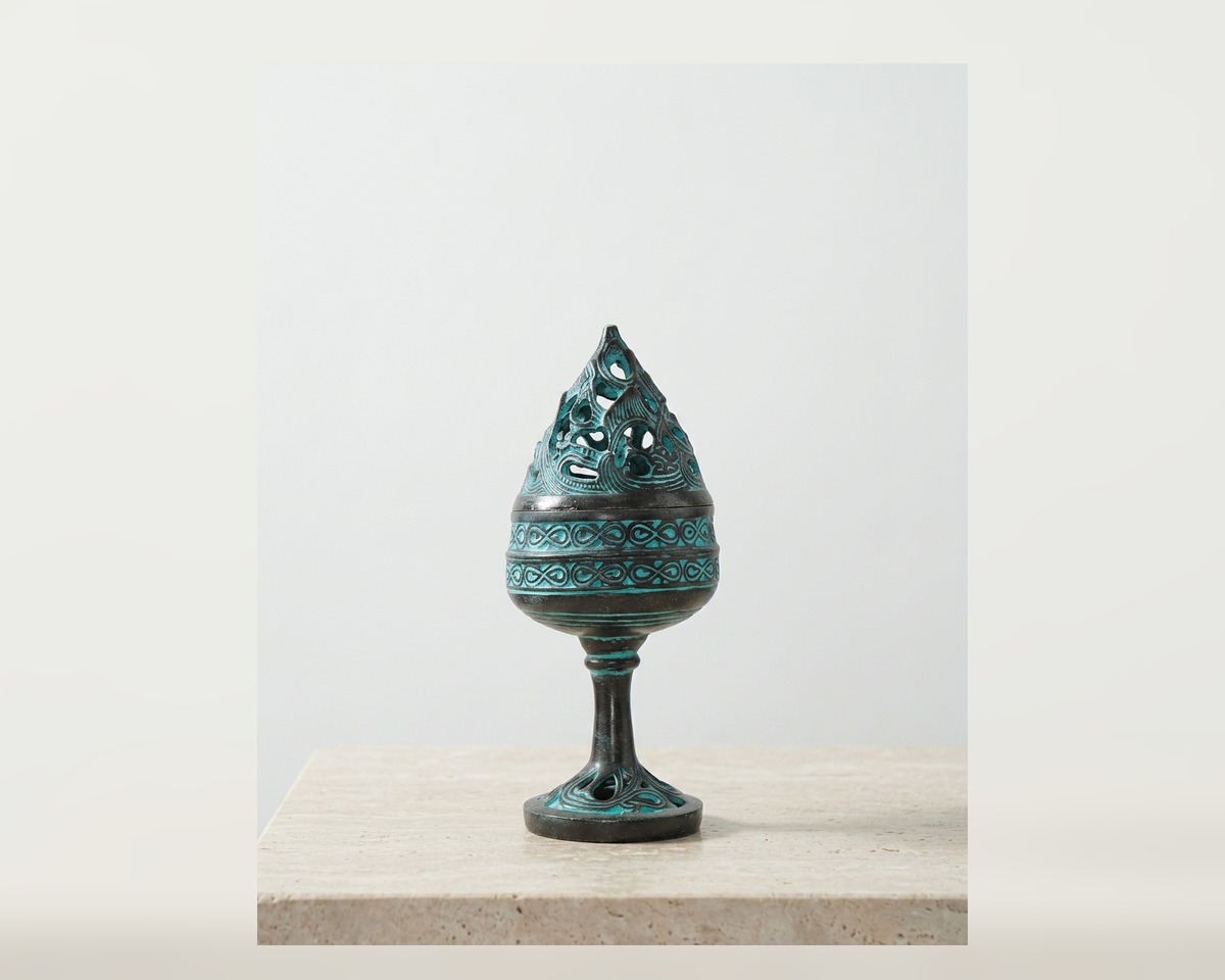 Miniature bronze incense burner with turquoise patina on a quiet mineral-white surface