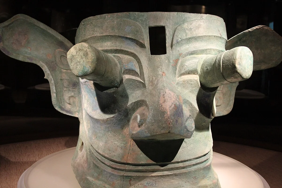 Sanxingdui bronze mask with protruding pupils and extended ears, photographed in a museum display